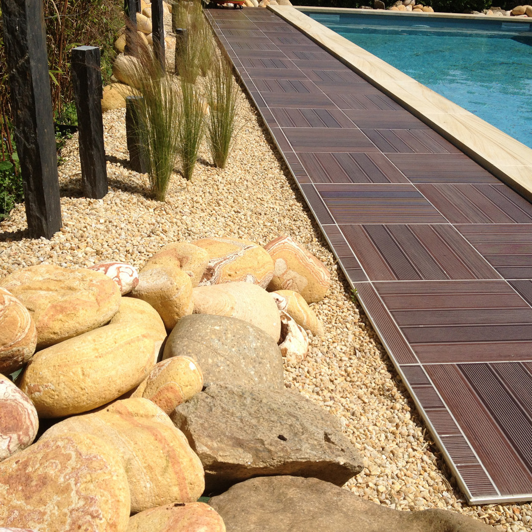 Piscine avec terrasse en bois et galets décoratifs.