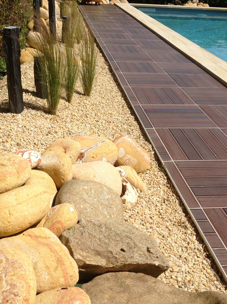 Piscine avec terrasse en bois et galets décoratifs.